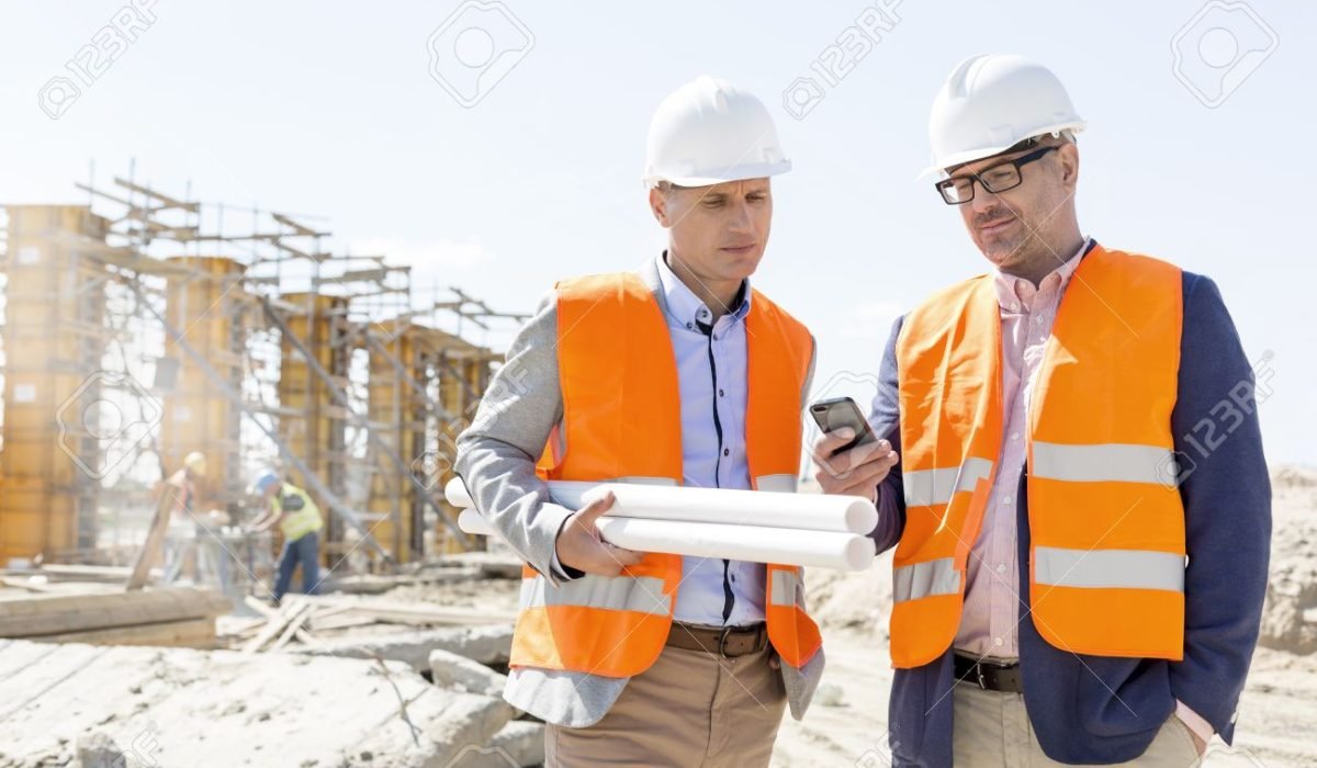 Male engineers using mobile phone at construction site against clear sky